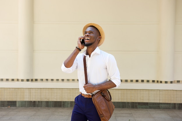 Young african guy standing on sidewalk with cellphone 