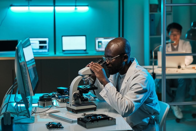 Young african laboratory worker looking in microscope