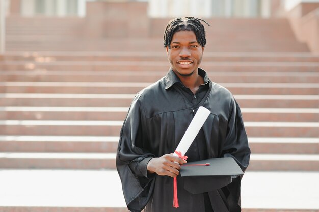 Young african male graduate standing in front of university building