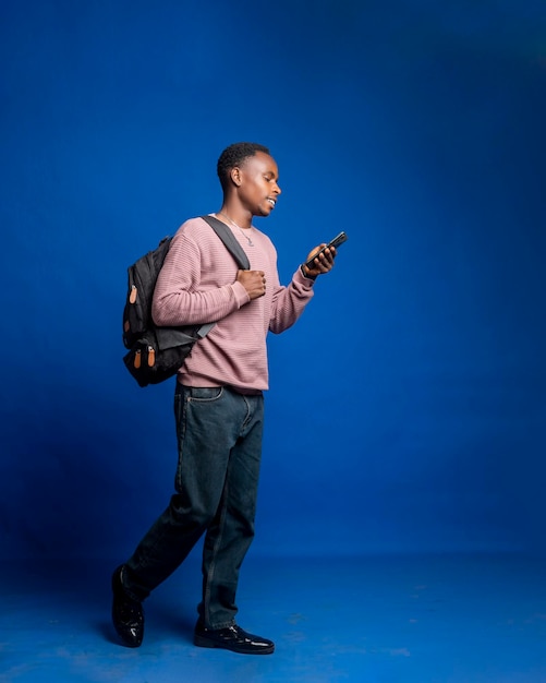 young African Male traveler carrying personal luggage bag standing on blue background