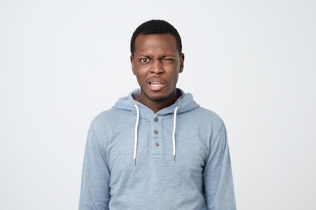 Young african man in blue shirt with puzzled expression on white background