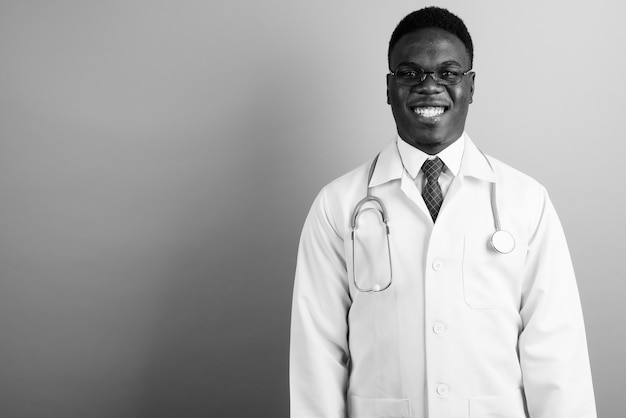 young African man doctor wearing eyeglasses against white wall. black and white