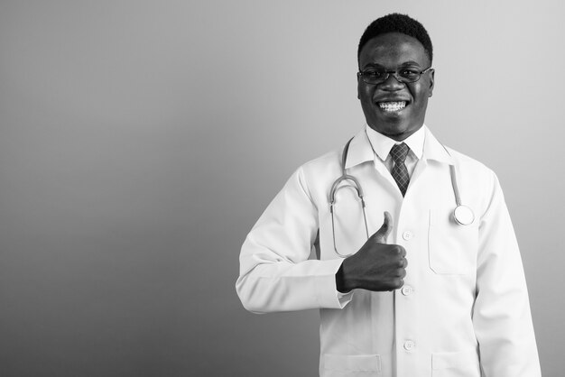 young African man doctor wearing eyeglasses against white wall. black and white