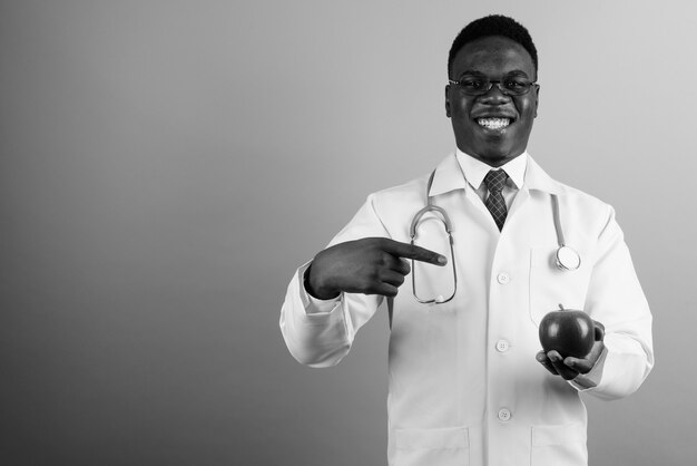 young African man doctor wearing eyeglasses against white wall. black and white