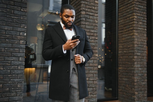 Молодой африканский мужчина в формальной одежде с помощью мобильного телефона