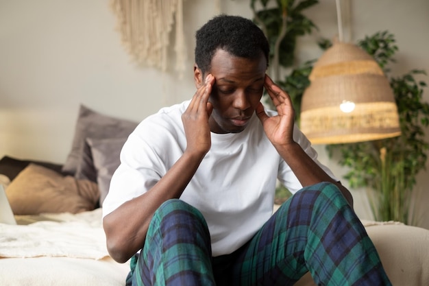 Young african man having headache sitting on bed in the morning