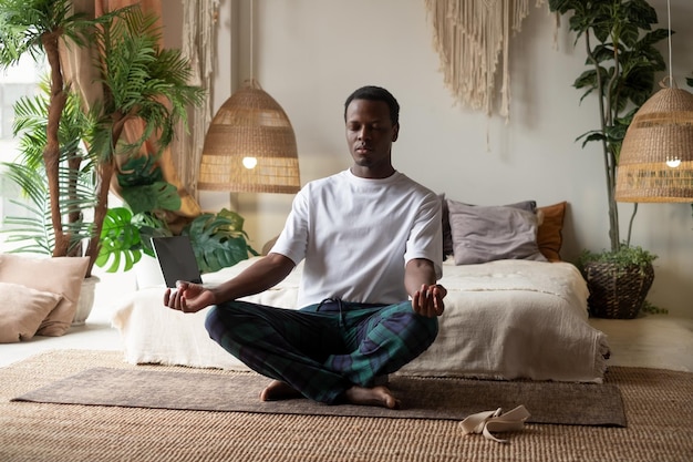 Young african man meditating sitting at his bedroom in the morning alone