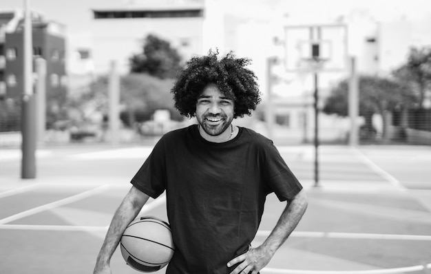 Young african man smiling on camera while holding basketball outdoor Black and white editing