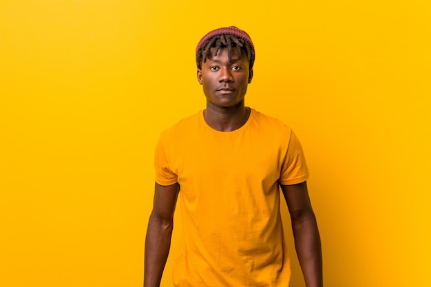 Young african man standing against a yellow wall wearing a hat