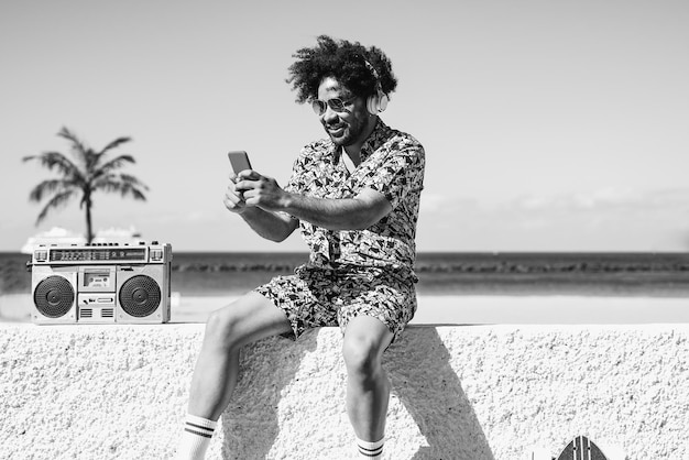 Young african man using mobile phone on the beach while listeing music playlist