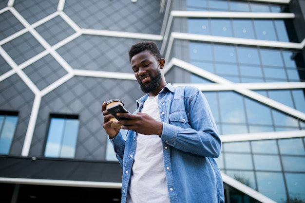 Il giovane africano che cammina sulla strada usa il telefono