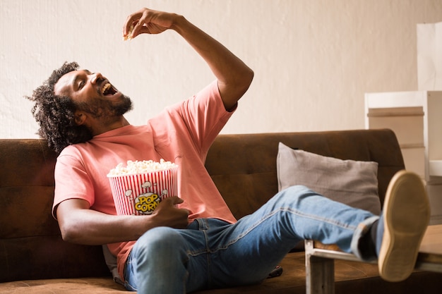 Young african man watching a movie holding a popcorn bucket.