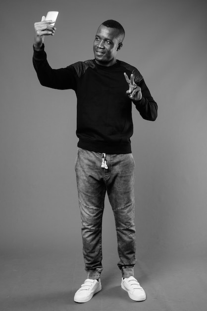 young African man wearing black long sleeved shirt against gray wall. black and white