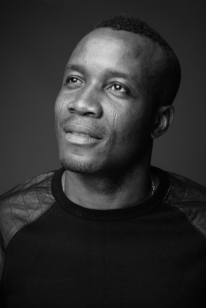 young African man wearing black long sleeved shirt against gray wall. black and white