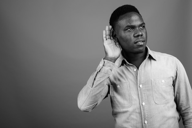 young African man wearing denim shirt against gray wall. black and white