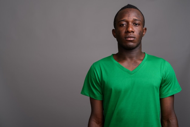 Young African man wearing green shirt on gray wall