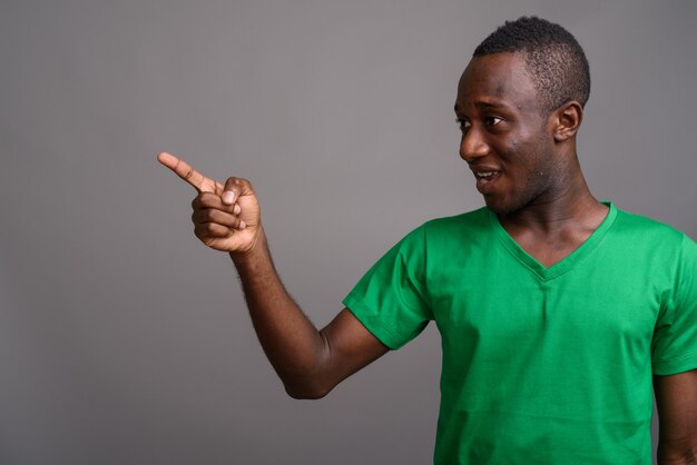 Young African man wearing green shirt on gray wall