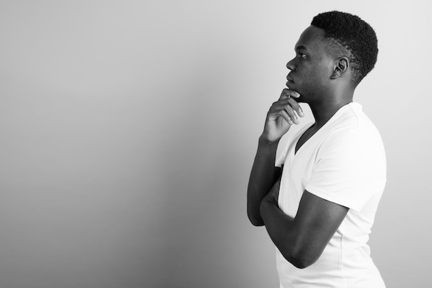 young African man wearing white shirt against white wall. black and white