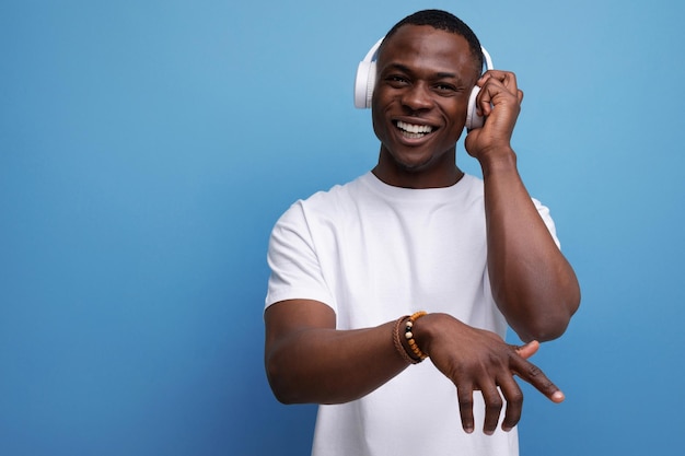 Young african man in white tshirt listening to music with white headphones on studio background with