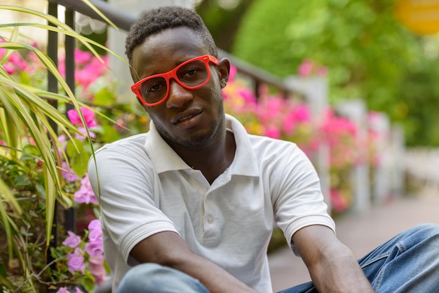 屋外の公園に座っている眼鏡をかけた若いアフリカ人