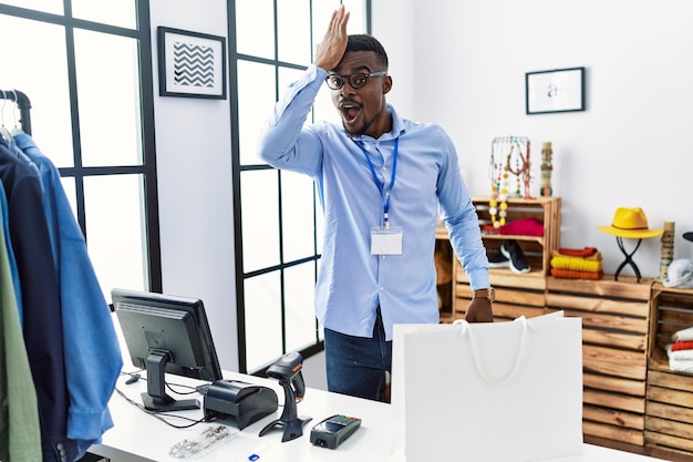 Young african man working as manager at retail boutique surprised with hand on head for mistake, remember error. forgot, bad memory concept.