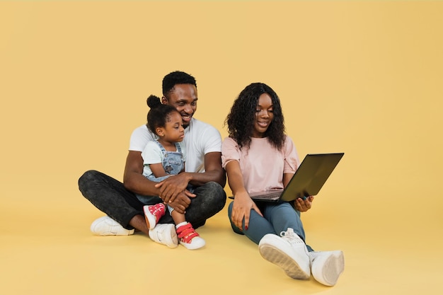 Young african parents sitting on floor with their daughter and embracing using laptop for video call