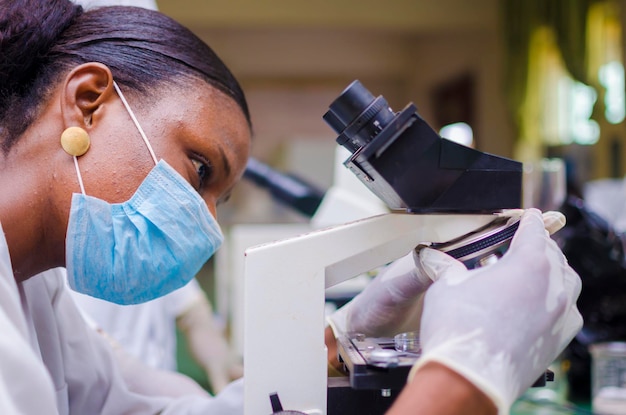 Молодой африканский ученый смотрит в микроскоп в лаборатории на вакцину, над которой она работает.