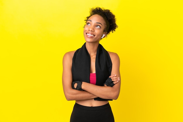 Young african sport woman isolated on yellow background looking up while smiling