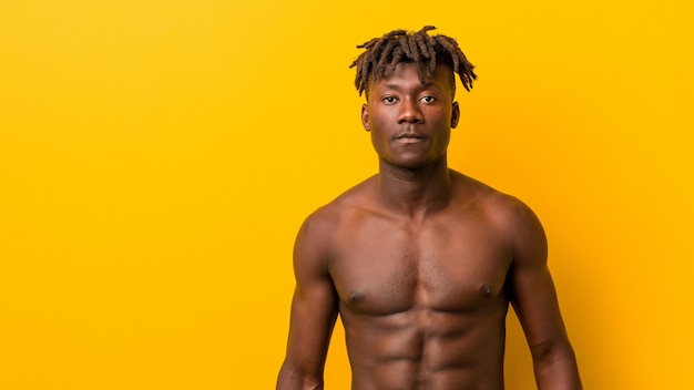 Молодой африканский спортивный человек стоял против желтой без футболки