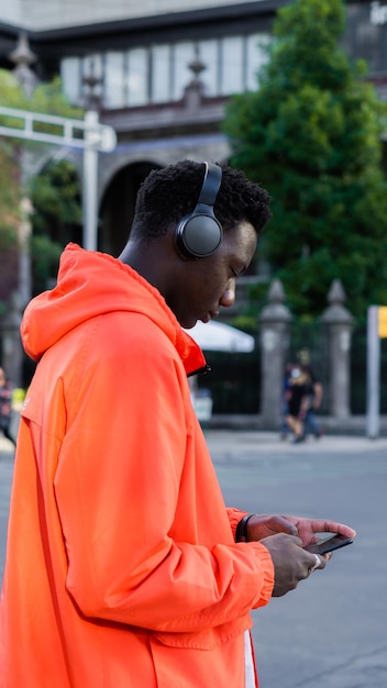 Young African texting on cell phone, listening to music with headphones in the city.