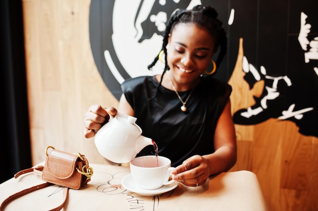 カフェで黒いブラウスを着た若いアフリカ人女性がティーポットからお茶を飲む