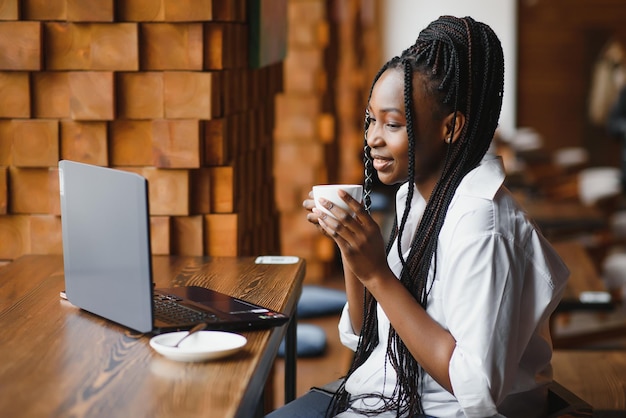 Giovane donna africana al caffè che beve caffè