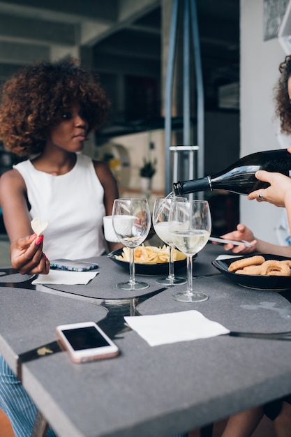 Молодая африканская женщина пьет вино в современном ресторане с друзьями