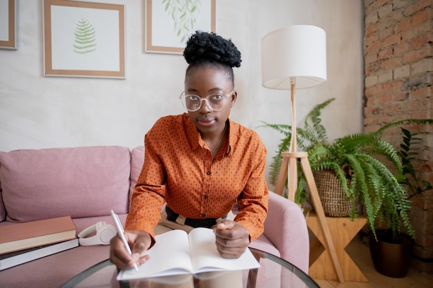 Photo young african woman in eyeglasses making notes in copybook