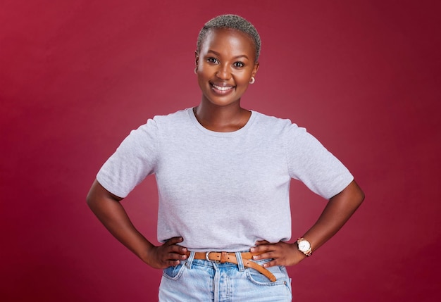 Young african woman and hands on hips in studio for beauty fashion and style with happiness Happy black woman portrait pose or smile face against red background for cosmetics makeup or glow skin