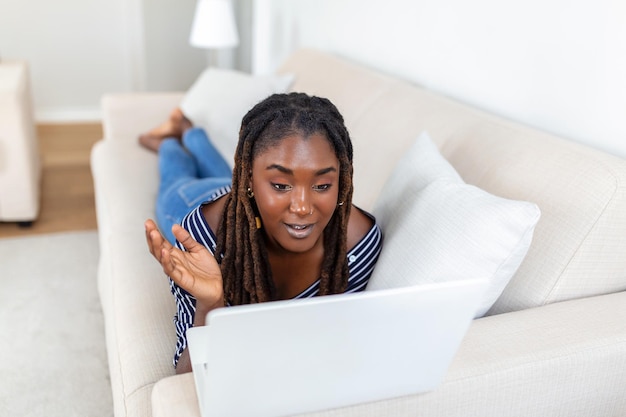 Young African woman having online video chat with friends via laptop with coffee cup in hand surprised expression Woman can't believe talking with family on video call