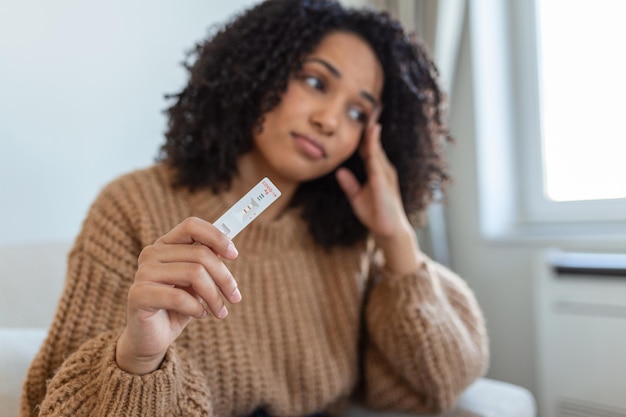 Young African woman holding positive Coronavirus  Covid19 rapid test Young African American woman taking a Selfswabbing home tests for COVID19 at home with Antigen kit