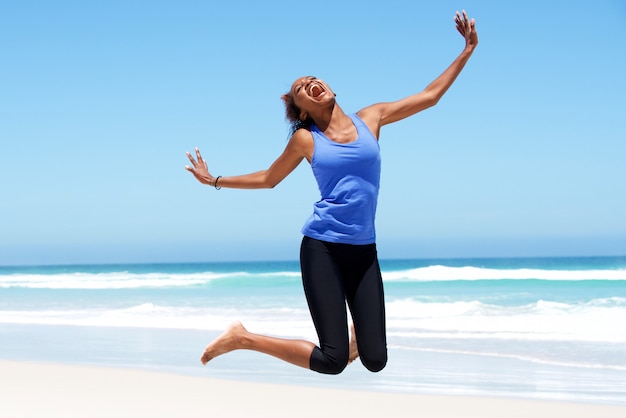 Young african woman jumping with joy at the beach