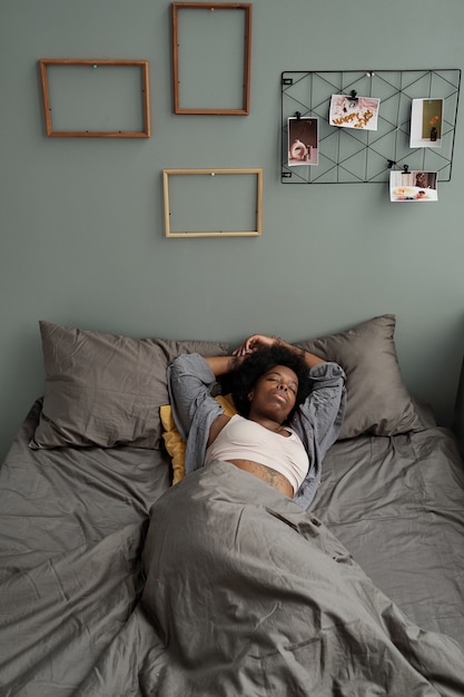 Young african woman lying under blanket in bed