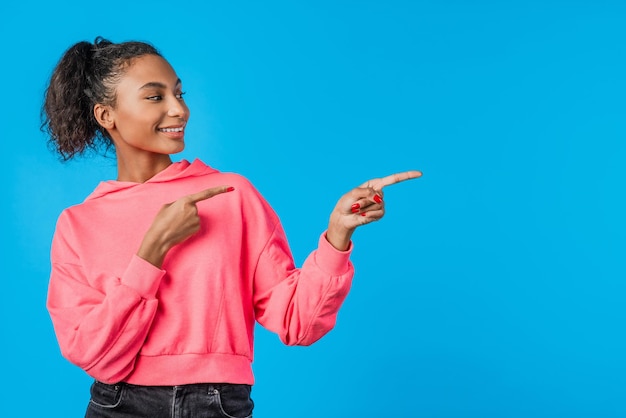 Young african woman pointing fingers at copy space isolated over blue background