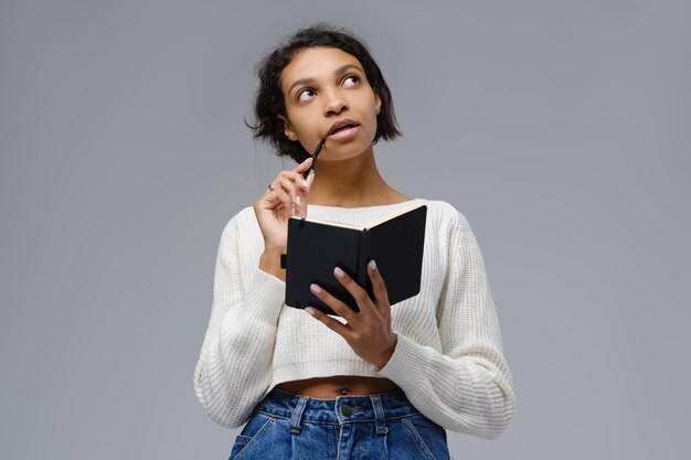 Young african woman recalls past events to write in a diary looks up