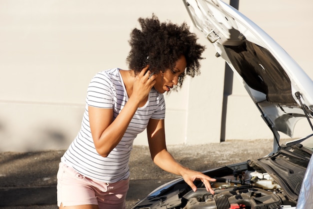 若いアフリカの女性が壊れた車で立って道路に駐車し、援助を呼び出す