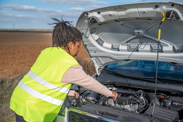 Young african woman standing by broken down car parked on the road