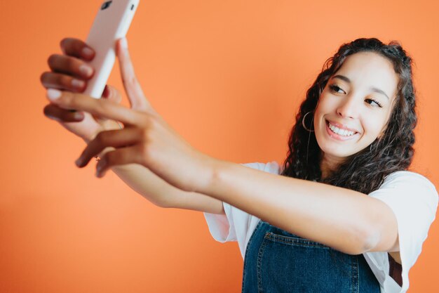 Photo young african woman taking a selfie while smiling, orange colour background, removable background, minimal reactions and expressions, young and happy person