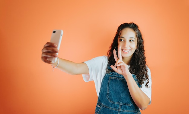 Young african woman taking a selfie while smiling, orange colour background, removable background, minimal reactions and expressions, young and happy person