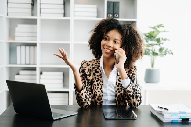 Young african woman typing on tablet and laptop while sitting at the working black table modern office