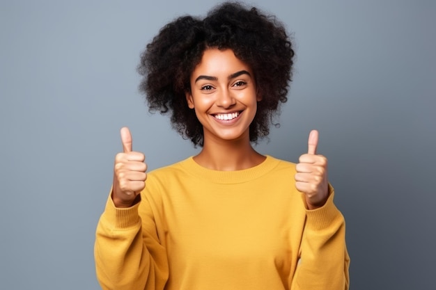 A young african woman in a yellow sweater is giving a thumbs up sign.