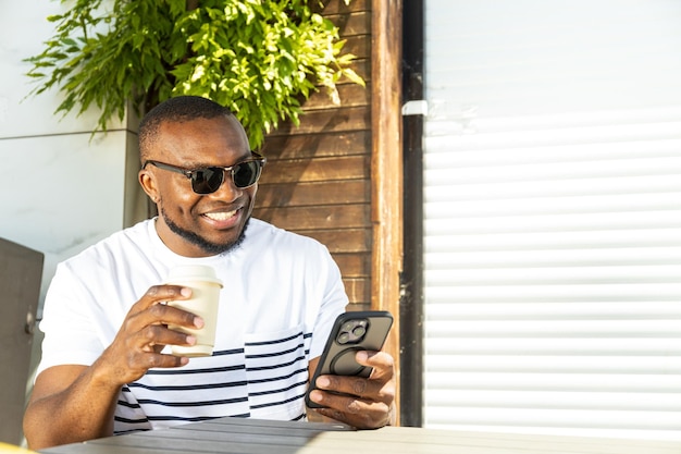 Photo a young africanamerican man with a smartphone and coffee