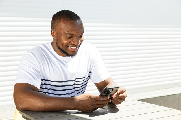 A young AfricanAmerican man with a smartphone in his hands is sitting at a table