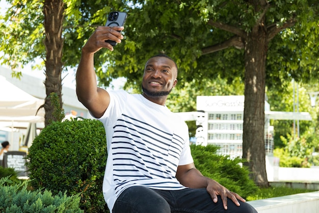 스마트폰을 가진 젊은 아프리카계 미국인 남자가 공원 벤치에 앉아 있다.